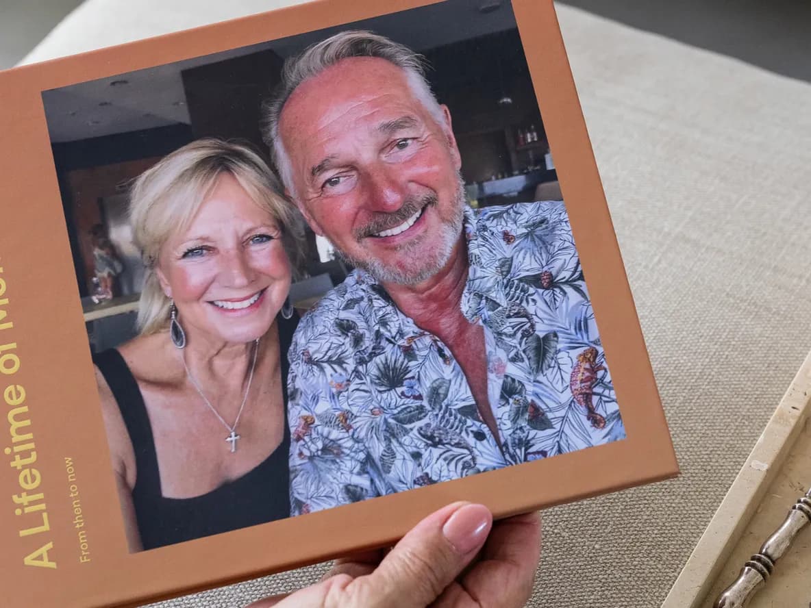 A person holds a photo album titled "A Lifetime of Memories" with a smiling couple on the cover. Nearby is a lit candle on a tray.