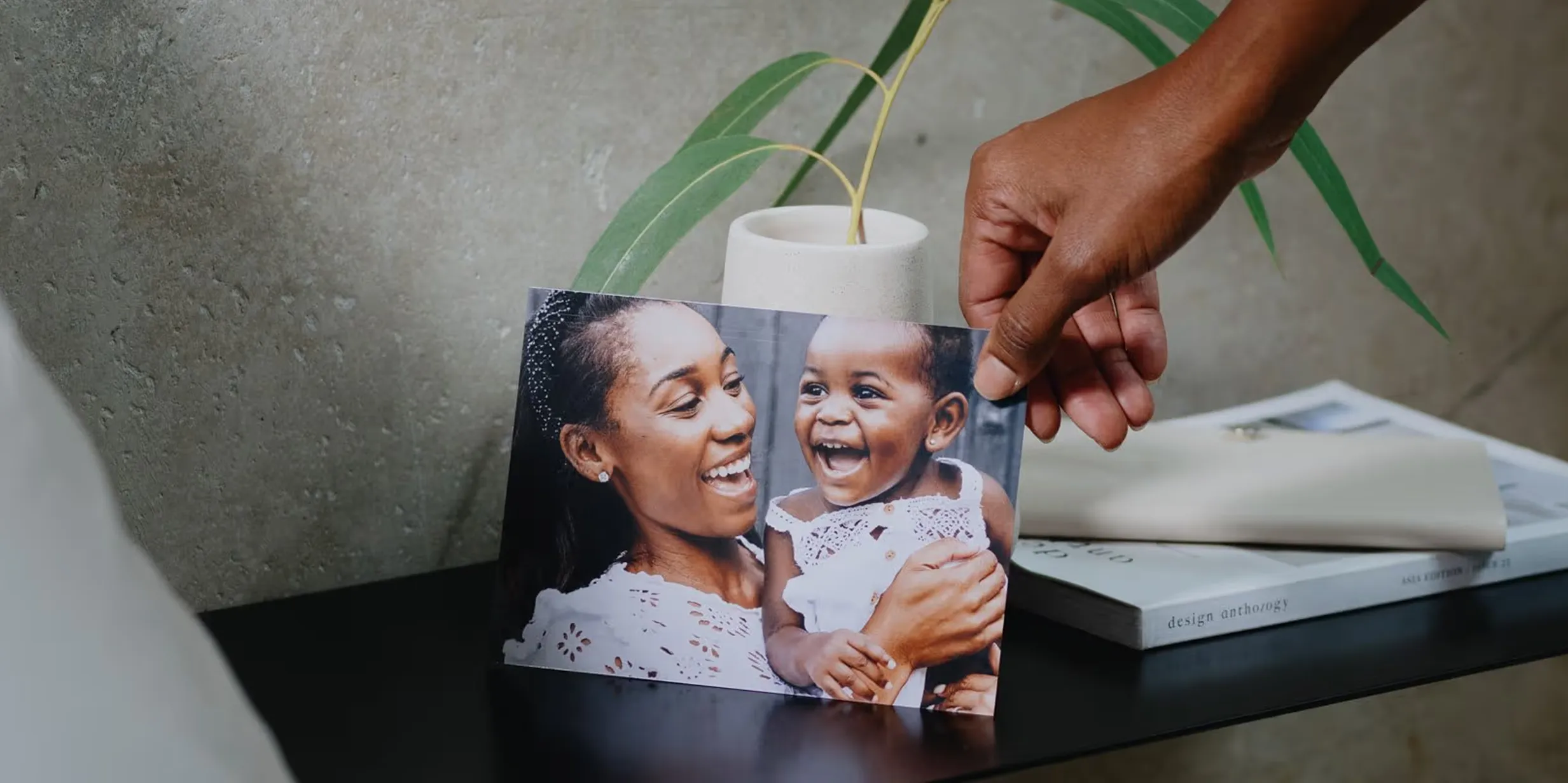 Dark-skinned hand places a photo of a joyful Black mother smiling with her laughing baby onto a dark shelf.