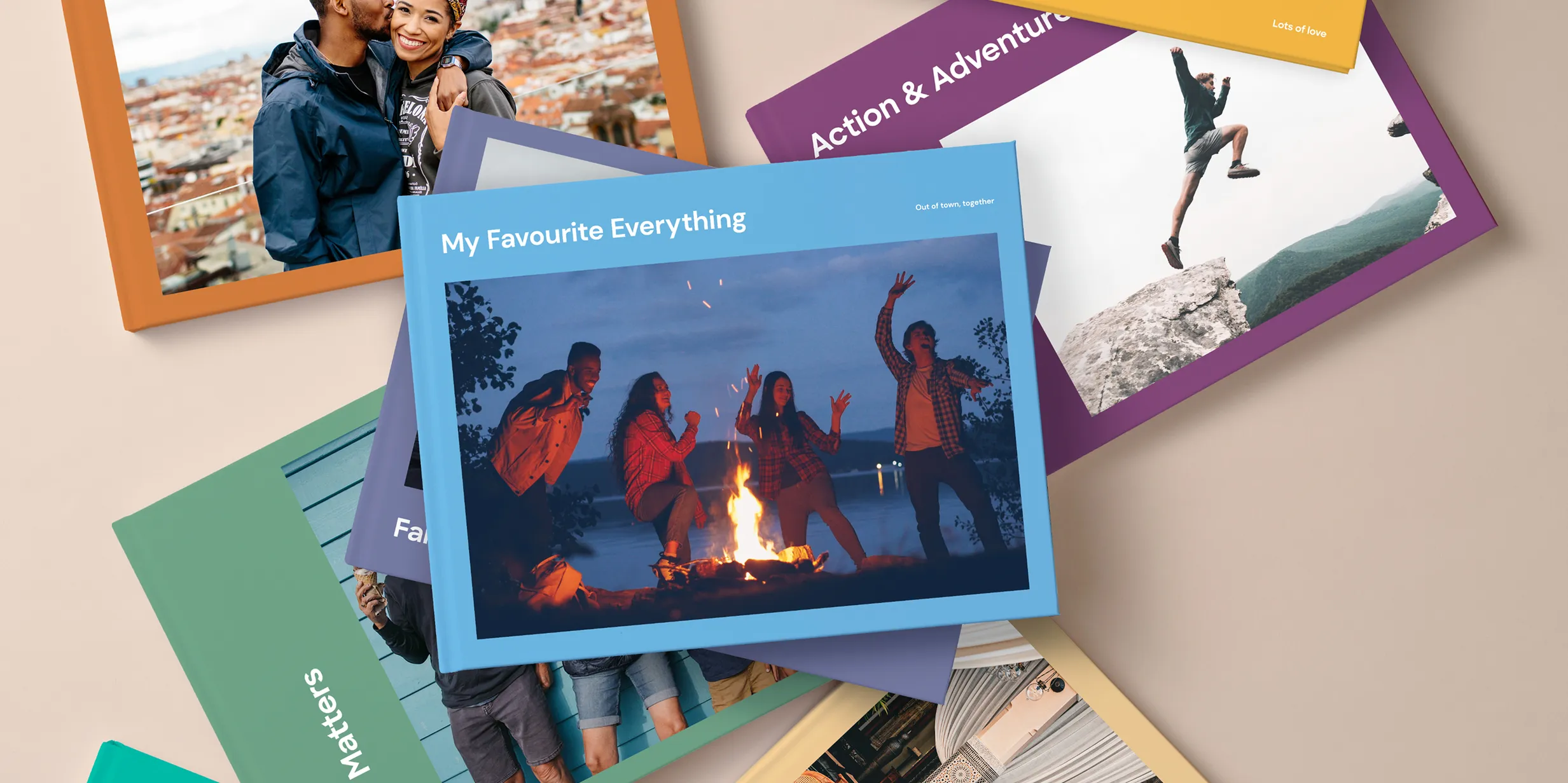 Stack of photo books with various covers, including a couple, a campfire scene, and people jumping on rocks, against a beige background.