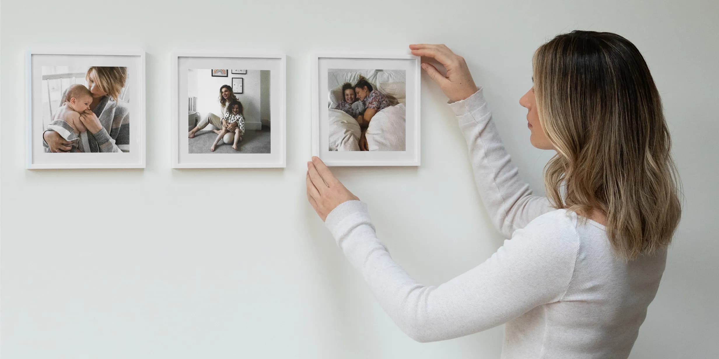 A woman hangs a framed photo of a mother and child sleeping on a white wall, completing a gallery of family moments.