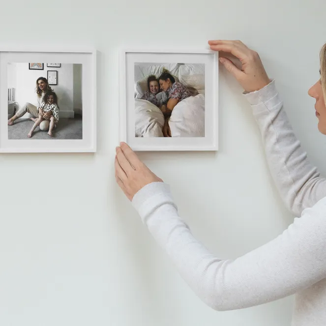 A woman hangs a framed photo of a mother and child sleeping on a white wall, completing a gallery of family moments.