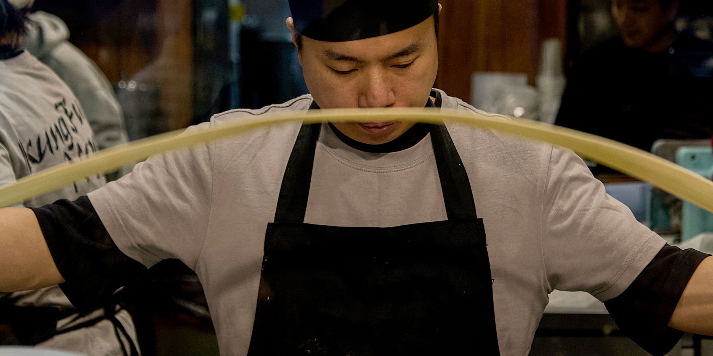 A chef in a black apron and hat stretches dough.
