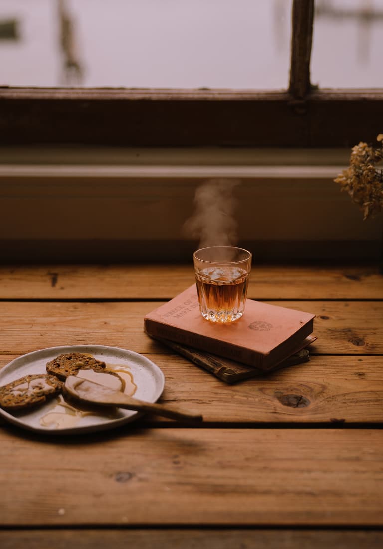 Steam rises from a glass of herbal tea alongside a plate of toast