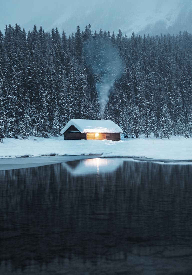 A cosy cottage on the shores of a lake wrapped with snowy trees
