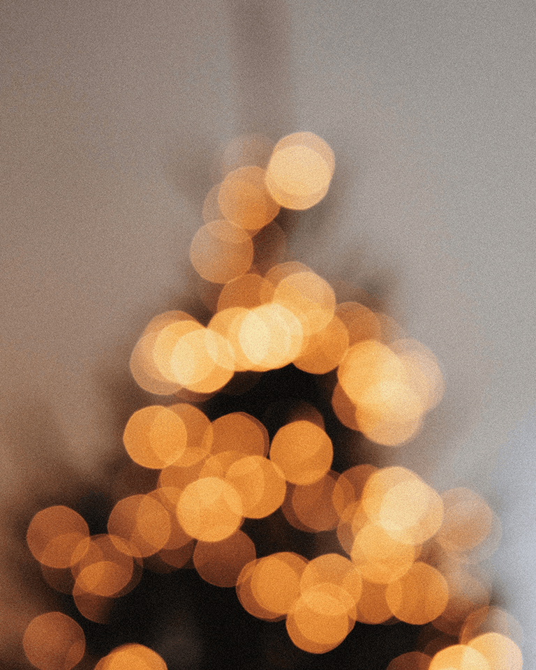 A blurry image of warm, glowing, yellow-orange lights arranged in a triangle pattern, resembling a decorated Christmas tree.