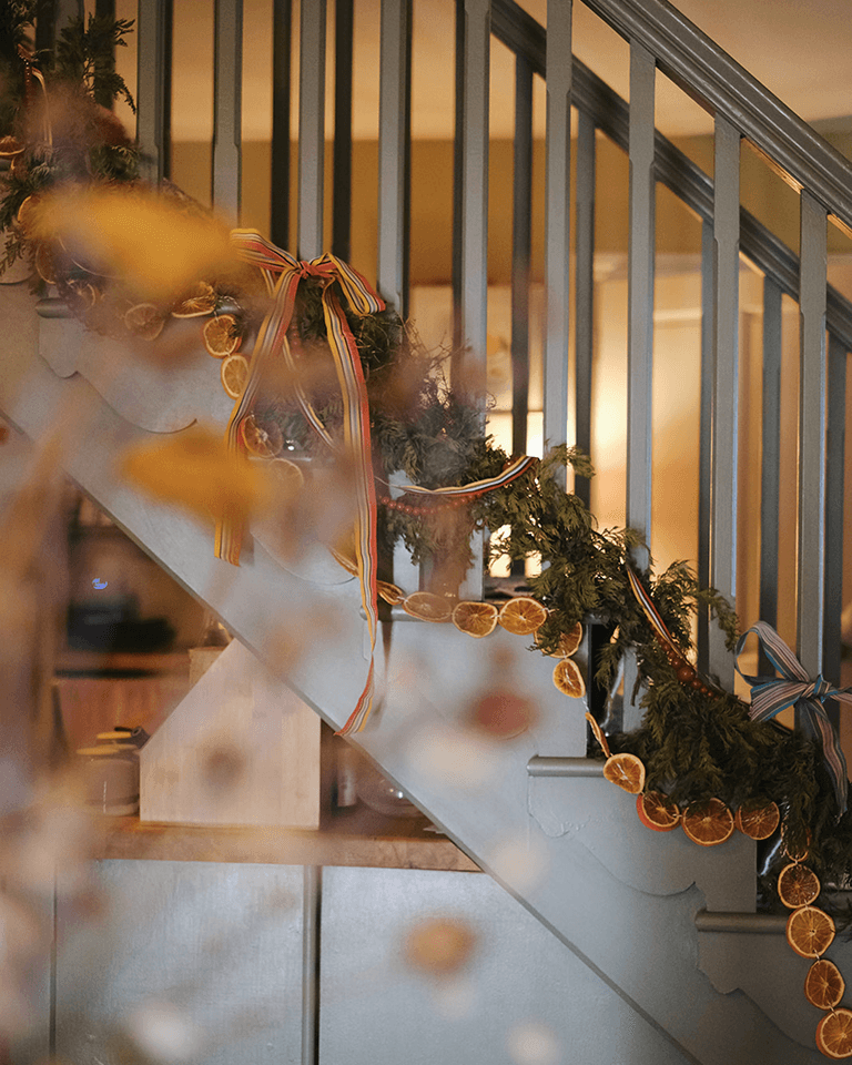A staircase adorned with evergreen garland, dried orange slices, and colorful ribbons, creating a festive and cozy atmosphere.