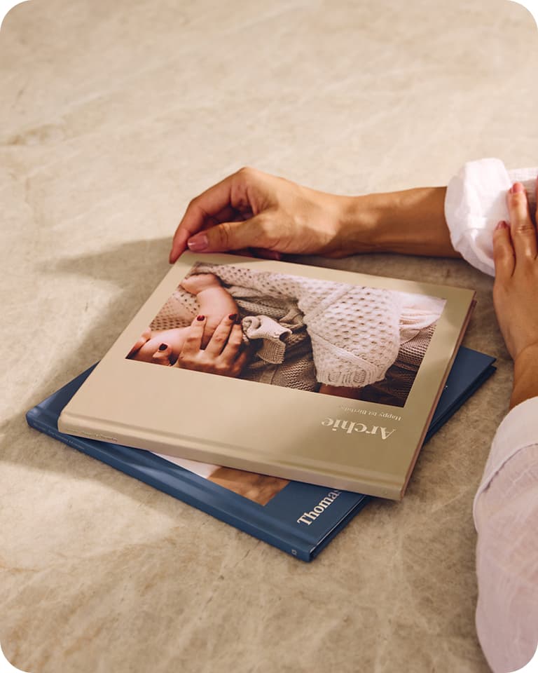 Hands resting on a table beside two photo books, one titled "Archie" with a cover image of a baby.
