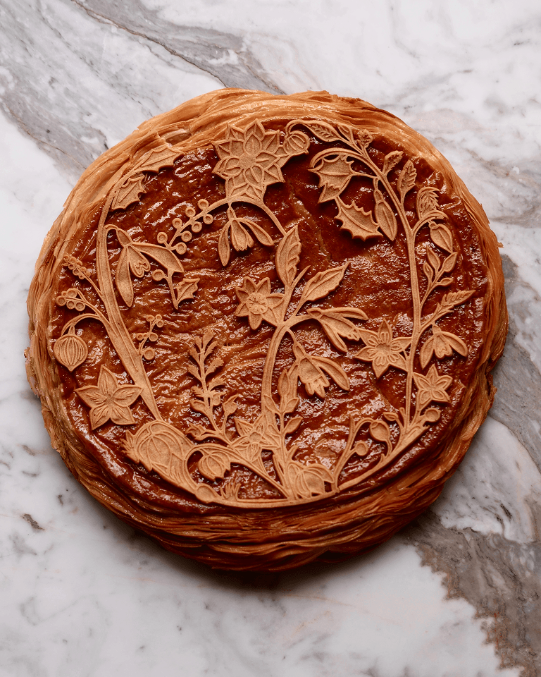 Intricately designed pastry with floral patterns on a marbled surface, showcasing detailed flowers and leaves in a circular arrangement.