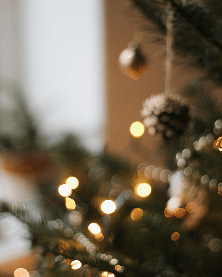 Blurred close-up of a Christmas tree with glowing lights, ornaments, and a pinecone in soft focus, creating a warm, festive atmosphere.