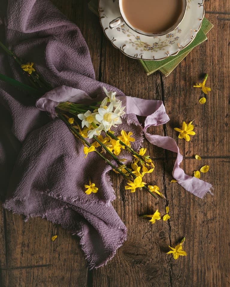 yellow flowers on a table with a cup of tea
