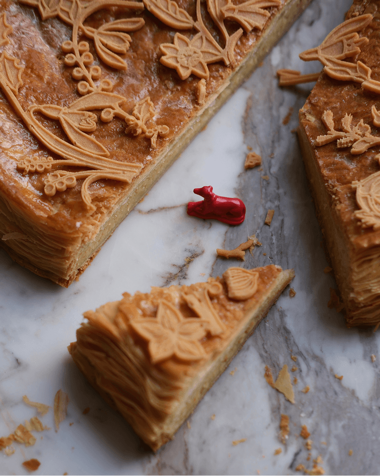 Decorative sliced pie with intricate floral designs on top, placed on marble. A small red figurine is beside the pie pieces.