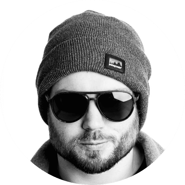 Man wearing sunglasses, a gray beanie, and a jacket, with a neutral expression, in a black and white portrait.